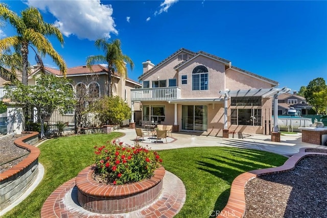 rear view of house featuring fence, a pergola, stucco siding, a balcony, and a yard