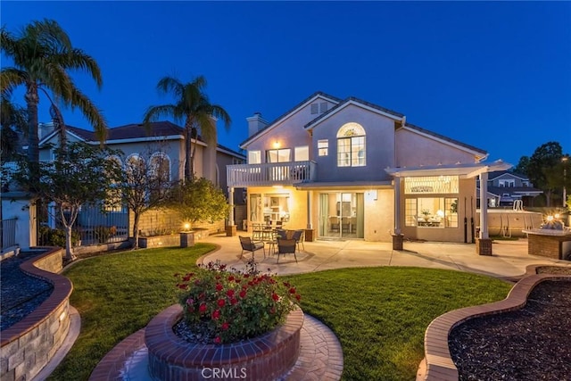 back of house at twilight with a yard, a balcony, and a patio area