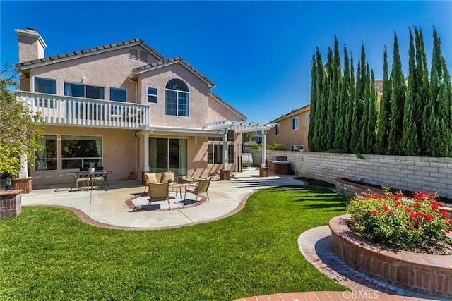 rear view of property featuring a chimney, a balcony, a yard, a pergola, and stucco siding