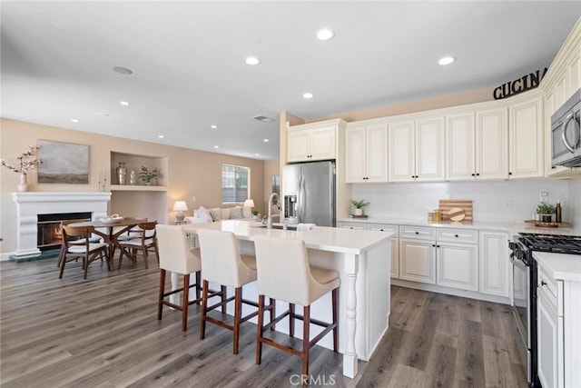 kitchen with a kitchen island with sink, light countertops, open floor plan, stainless steel appliances, and dark wood-type flooring
