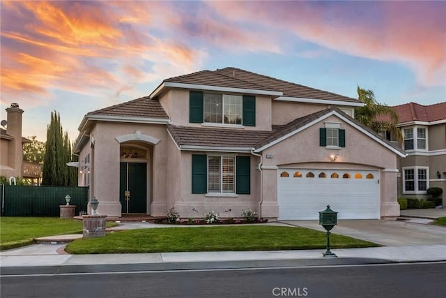 traditional-style home with a lawn, fence, stucco siding, concrete driveway, and an attached garage