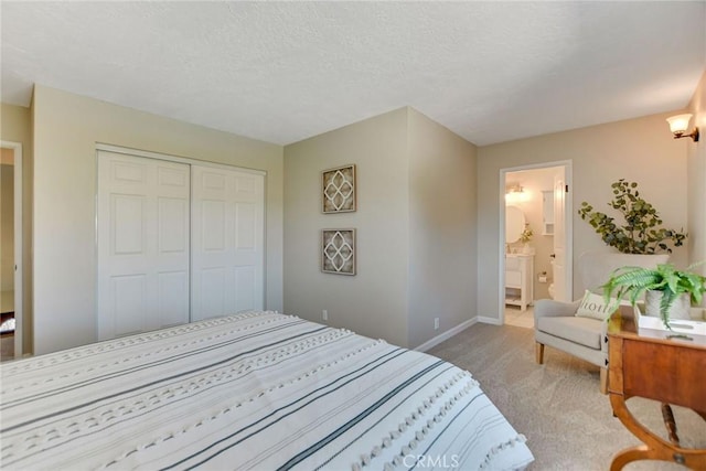 bedroom with a textured ceiling, light colored carpet, baseboards, a closet, and ensuite bath