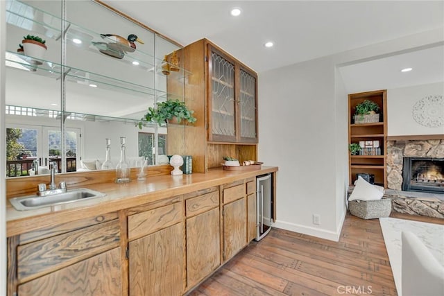 bar featuring wine cooler, a fireplace, light wood-type flooring, recessed lighting, and a sink