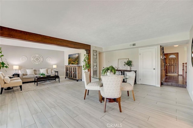 dining space with beamed ceiling, visible vents, and light wood-style flooring