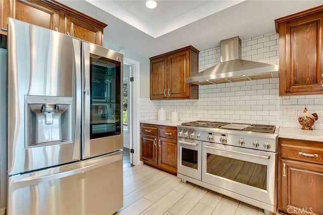 kitchen featuring wall chimney range hood, appliances with stainless steel finishes, decorative backsplash, and light countertops