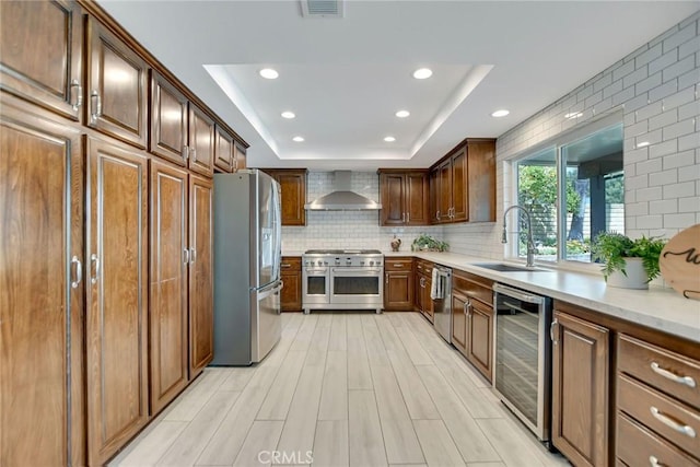 kitchen featuring appliances with stainless steel finishes, a sink, wine cooler, recessed lighting, and wall chimney exhaust hood