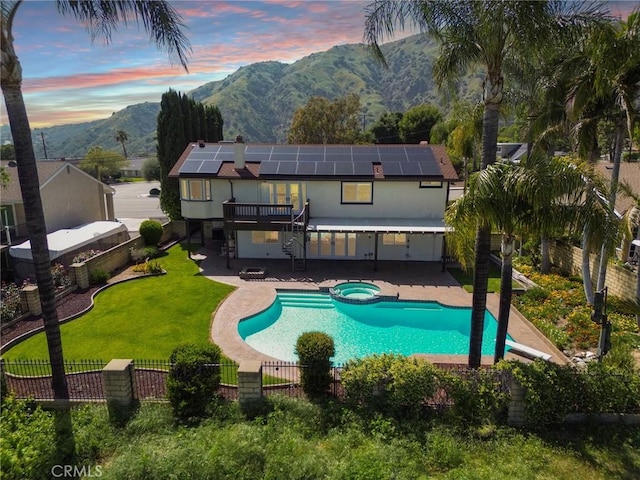 back of property at dusk featuring a fenced backyard, a mountain view, solar panels, a patio, and a yard