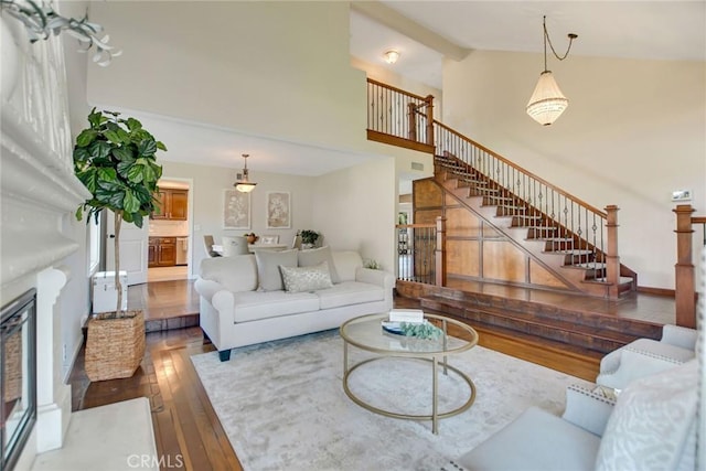 living area with visible vents, hardwood / wood-style flooring, high vaulted ceiling, a glass covered fireplace, and stairs