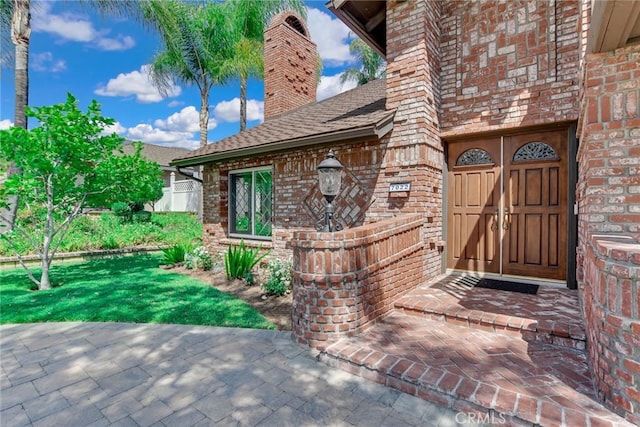 doorway to property with brick siding, roof with shingles, and a chimney