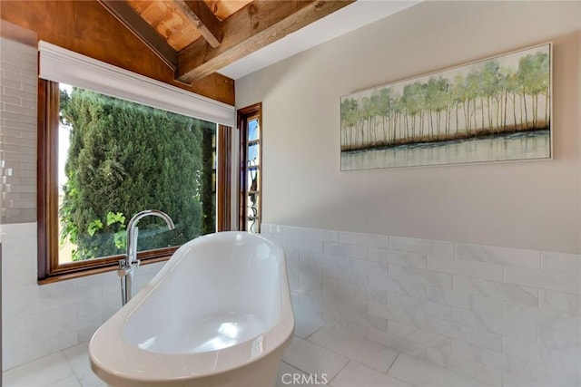 full bath featuring a freestanding bath, tile walls, plenty of natural light, and beam ceiling