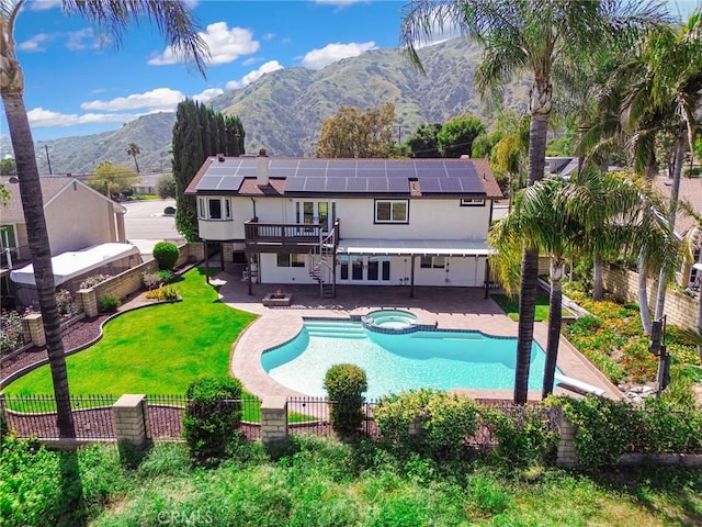 rear view of house with a fenced backyard, a patio area, a mountain view, a pool with connected hot tub, and solar panels