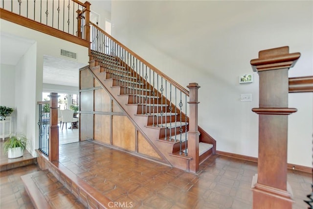staircase featuring a towering ceiling, baseboards, decorative columns, and visible vents