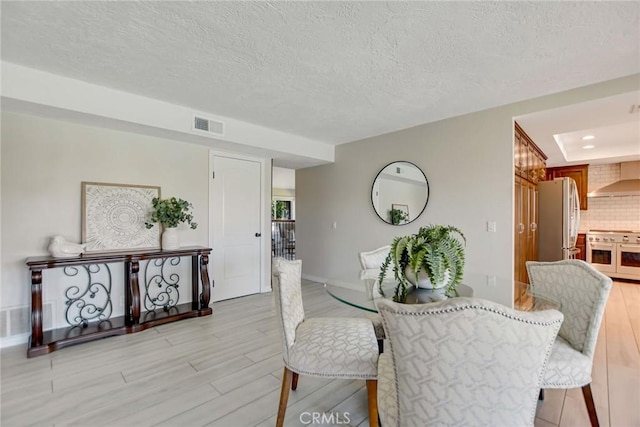 dining space with baseboards, light wood-type flooring, a textured ceiling, and visible vents