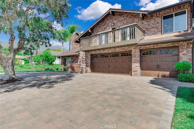 view of front of home with a balcony, a garage, decorative driveway, and brick siding