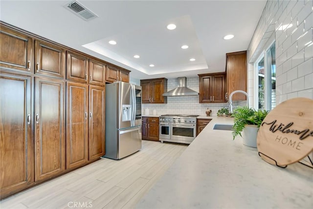 kitchen with visible vents, wall chimney exhaust hood, a tray ceiling, a sink, and stainless steel appliances