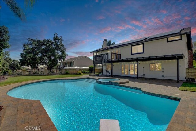 view of swimming pool featuring a diving board, a pool with connected hot tub, a wooden deck, stairway, and a patio area