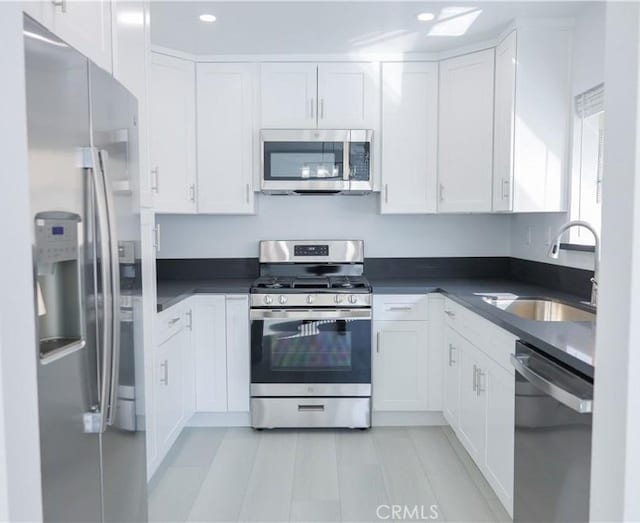 kitchen with dark countertops, appliances with stainless steel finishes, a sink, white cabinetry, and recessed lighting