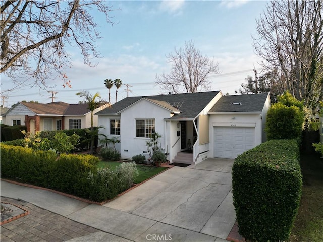 ranch-style home featuring an attached garage, driveway, a shingled roof, and stucco siding