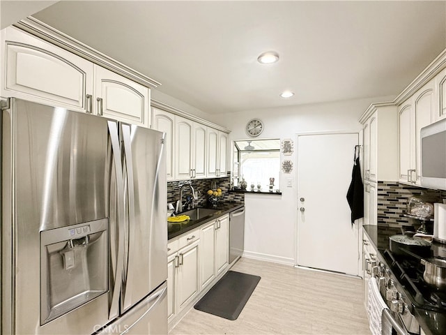 kitchen with a sink, appliances with stainless steel finishes, decorative backsplash, and dark countertops
