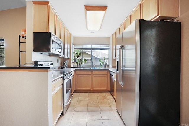 kitchen featuring a peninsula, light brown cabinets, dark countertops, a sink, and appliances with stainless steel finishes