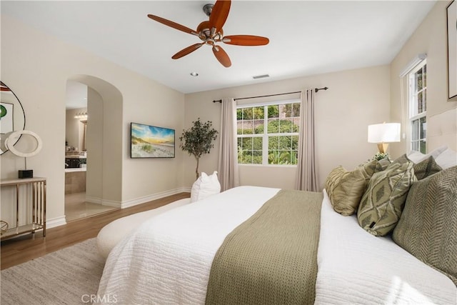 bedroom with arched walkways, a ceiling fan, baseboards, wood finished floors, and visible vents