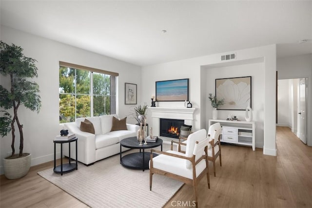 living room featuring wood finished floors, a glass covered fireplace, and baseboards
