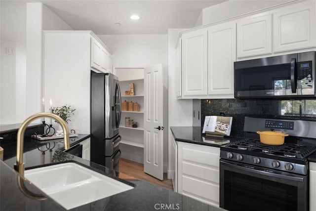 kitchen featuring appliances with stainless steel finishes, a sink, white cabinetry, decorative backsplash, and wood finished floors