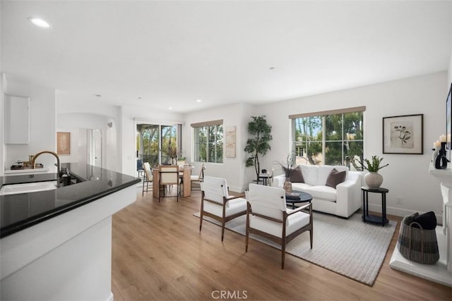 living room featuring light wood-style floors, recessed lighting, arched walkways, and baseboards