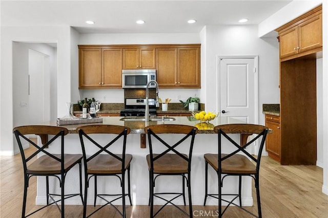 6410 Eucalyptus Ave, Chino, CA 91710 - kitchen featuring brown cabinetry, a kitchen island with sink, appliances with stainless steel finishes, a sink, and light wood finished floors