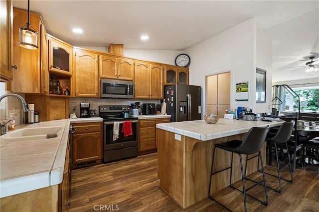 kitchen featuring brown cabinetry, decorative backsplash, tile counters, a sink, and appliances with stainless steel finishes