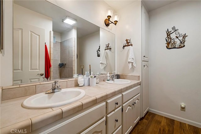 full bathroom with double vanity, a sink, baseboards, and wood finished floors