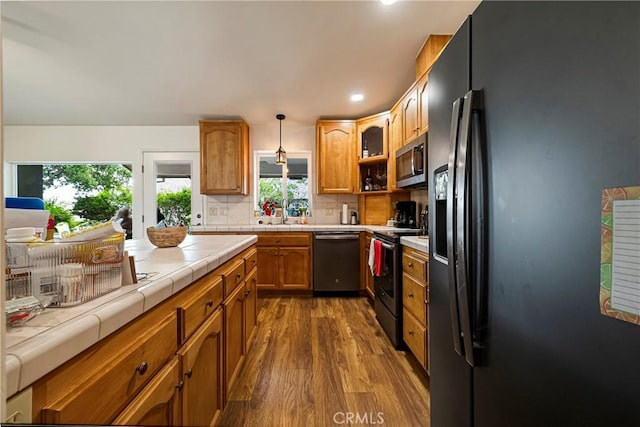 kitchen featuring dark wood-style floors, tile countertops, brown cabinets, appliances with stainless steel finishes, and backsplash