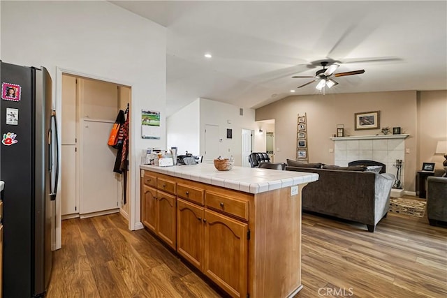 kitchen with brown cabinets, freestanding refrigerator, a ceiling fan, a peninsula, and wood finished floors