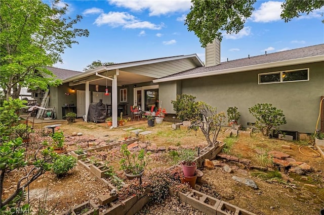 back of house featuring stucco siding, a garden, a patio area, and a chimney