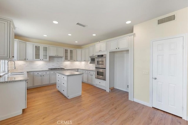 27020 Island Rd, Valencia, CA 91355 - kitchen featuring stainless steel appliances, tasteful backsplash, light wood-style floors, a center island, and glass insert cabinets