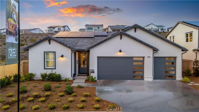 view of front facade featuring concrete driveway, an attached garage, roof mounted solar panels, and stucco siding