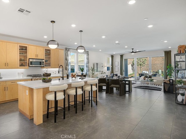 kitchen with a ceiling fan, visible vents, appliances with stainless steel finishes, light brown cabinets, and an island with sink