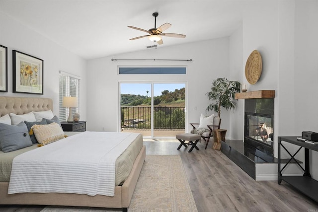 bedroom with a ceiling fan, a fireplace, wood finished floors, lofted ceiling, and access to outside