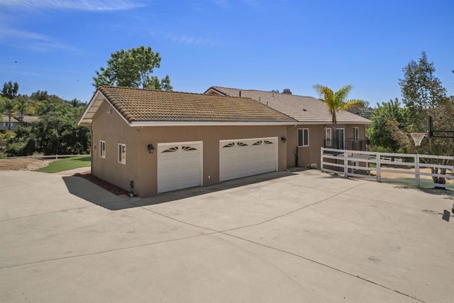 view of home's exterior with fence, a garage, stucco siding, concrete driveway, and a tiled roof
