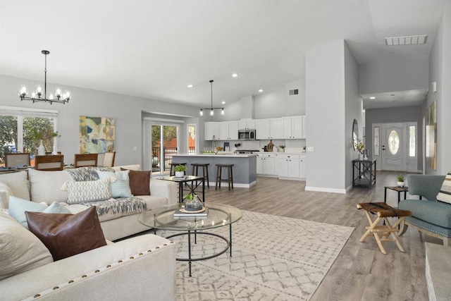 living room featuring light wood-style floors, a notable chandelier, a wealth of natural light, and visible vents