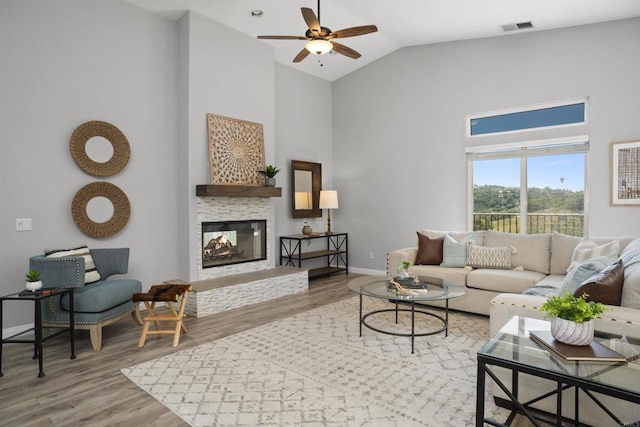 living area featuring visible vents, wood finished floors, ceiling fan, high vaulted ceiling, and a multi sided fireplace