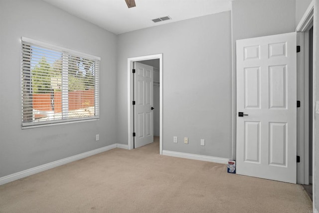 unfurnished bedroom with a walk in closet, a ceiling fan, visible vents, carpet floors, and baseboards