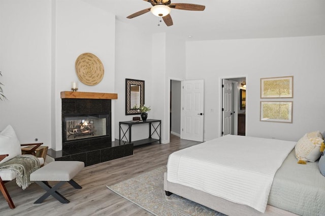 bedroom featuring ceiling fan, high vaulted ceiling, a tiled fireplace, baseboards, and wood finished floors