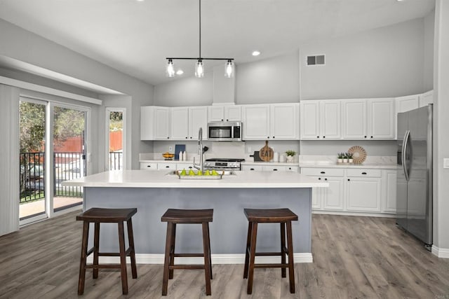 kitchen with a high ceiling, stainless steel appliances, white cabinetry, and visible vents