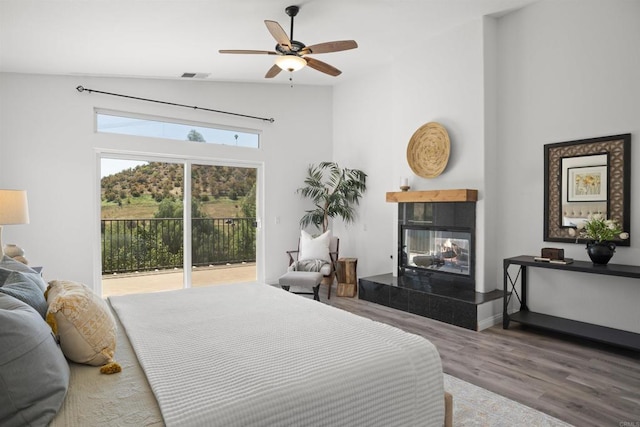 bedroom with visible vents, wood finished floors, a tile fireplace, lofted ceiling, and access to outside