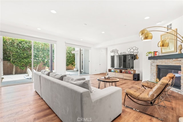 living area with light wood-style floors, a glass covered fireplace, and recessed lighting