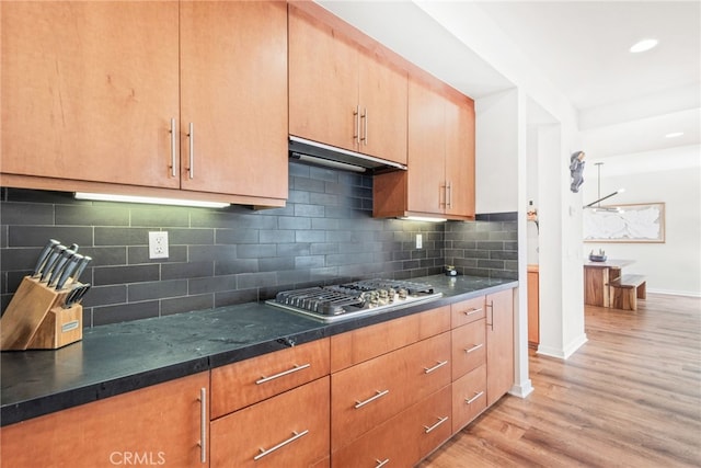 kitchen with under cabinet range hood, light wood-style floors, stainless steel gas cooktop, tasteful backsplash, and baseboards