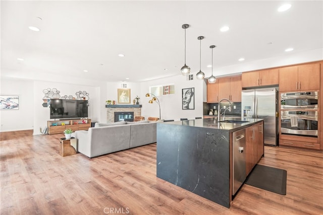 kitchen with appliances with stainless steel finishes, a sink, a fireplace, light wood-style flooring, and recessed lighting