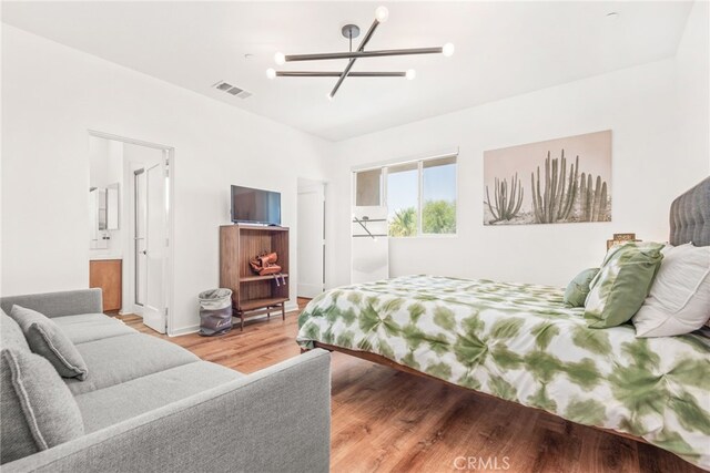 bedroom with a chandelier, light wood-style floors, ensuite bath, and baseboards