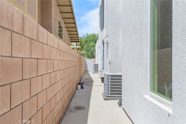 view of side of property with central AC, fence, and stucco siding